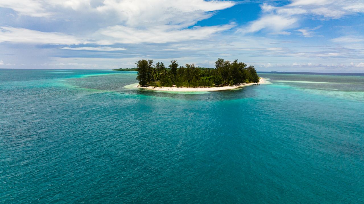 Aerial view of a tropical beach in Balabac, Palawan with clear turquoise water, palm trees, and boats, showing why travelers ask "is Balabac Palawan safe"
