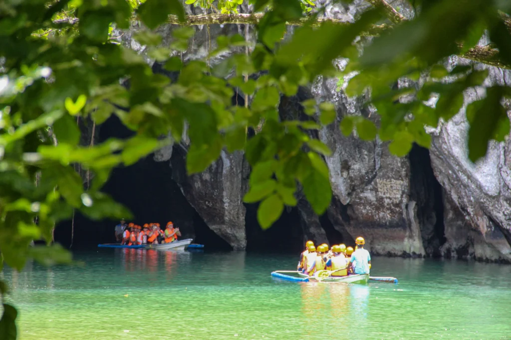 Tourists wearing life jackets and helmets ride in small boats near the cavernous limestone entrance of the underground river Palawan.