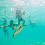 A group enjoying a family vacation in Palawan with little kids and non-swimmers wearing life jackets while snorkeling underwater alongside a green sea turtle.