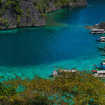 Boats docked in a clear turquoise lagoon, a scenic hub for Coron Palawan diving tours.