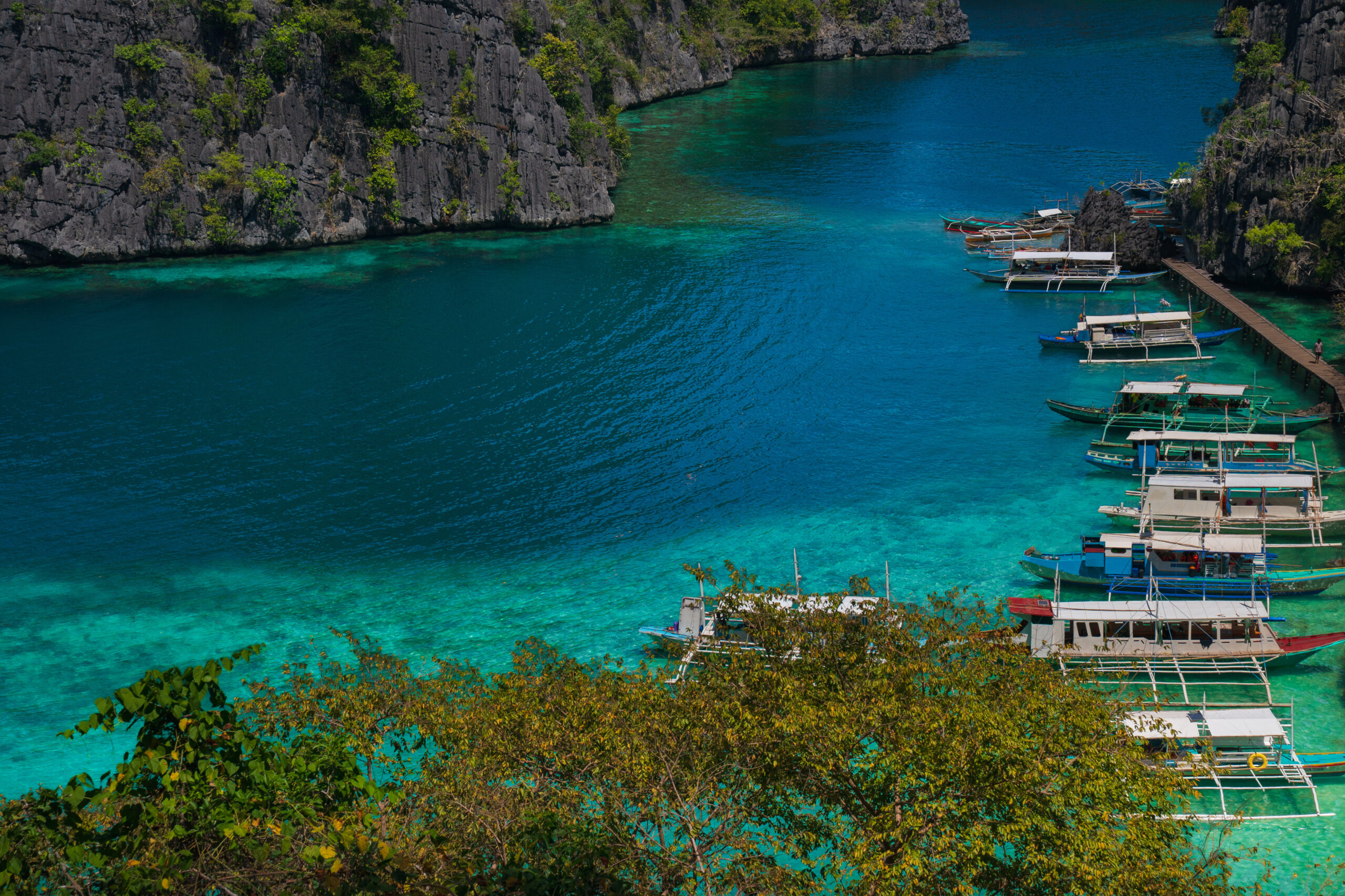 Boats docked in a clear turquoise lagoon, a scenic hub for Coron Palawan diving tours.